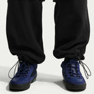 A person wearing Ishod Cargo Pant Sweatpant Black IF0659010 by Nike SB with drawstring ankles and dark blue sneakers, standing on a light background.