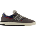A Castlerock navy New Balance Numeric Jamie Foy Cup 306 CYZ skateboarding shoe featuring a gray suede upper, white laces, a white rubber cup outsole for enhanced traction, and navy and red accents. Designed in collaboration with Jamie Foy, it showcases the signature “N” logo on the side.