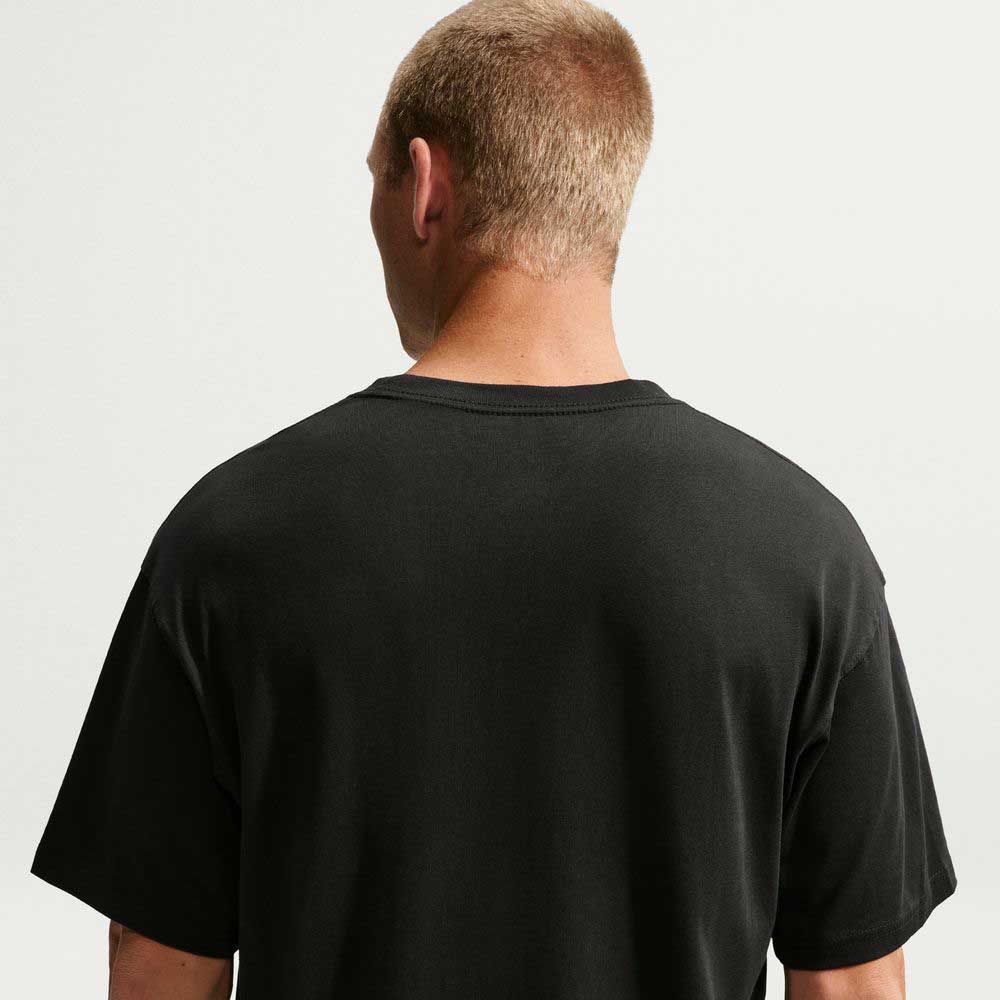 A person with short light brown hair is standing with their back to the camera, wearing a plain black Nike SB Skateboarding Cell Phone Tee (IM4424-010) T-shirt against a plain, light background.