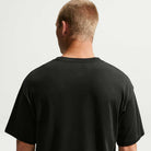A person with short light brown hair is standing with their back to the camera, wearing a plain black Nike SB Skateboarding Cell Phone Tee (IM4424-010) T-shirt against a plain, light background.