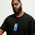 A man with a beard wears the Nike SB Skateboarding Cell Phone Tee Black IM4424010 T-Shirt, which features a blue retro mobile phone graphic on the front. Reminiscent of the comfort found in a Nike SB Jacquard Skate Jersey, this tee combines casual style with the feel of your favorite skate jersey top. The background is plain white.