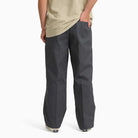 Wearing Charcoal Loose Fit Work Pant A88KB0CH Dickies Skateboarding, a person stands with one hand in their pocket, facing away. Only the lower half of their body is visible.