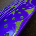 Close-up of a shiny surface with metallic purple and green patterns—curved lines and circular dots—evoking the graphics on the Chop Shop Flame 8.50in x 32.05in Creature Skateboard Shaped Deck made from 7 ply North American Maple. Softly blurred background.