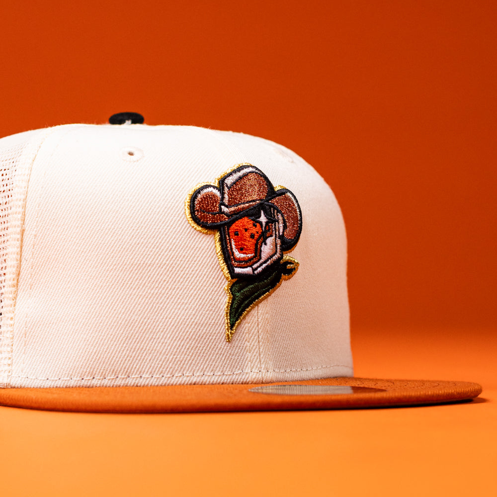 Introducing The Wrangler Chrome Rust Sugarland Space Cowboys New Era Hat 5950 Fitted—a white and orange trucker cap featuring an embroidered patch of a strawberry sporting a cowboy hat and bandana against an orange background. This lively design embodies the energetic spirit of the Space Cowboys Hat collection, making it ideal for anyone eager to add some playful flair to their collection.