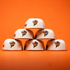 Six The Wrangler Chrome Rust Sugarland Space Cowboys New Era Hat 5950 Fitted caps are stacked in a pyramid shape against an orange background, reminiscent of the playful style found in classic New Era collections.