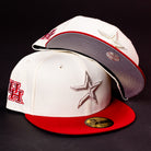 Two cream-colored The Carter Chrome Scarlet Houston Cougars New Era 5950 Fitted baseball caps with red brims. One showcases a bold red UH logo in tribute to the Houston Cougars, while the other features a striking silver star emblem. Both hats retain their original stickers and are set against a sleek black background.