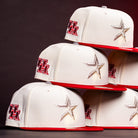 Stacked white and red “The Carter Chrome Scarlet Houston Cougars New Era Hat 5950 Fitted” caps, featuring a red UH logo on the side and a silver star on the front, are prominently displayed against a dark background.