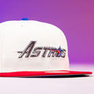 The Diplomat Chrome Scarlet Houston Astros New Era 5950 Fitted Hat is white with a red brim, blue button, and "Astros" embroidered in silver with a star, displayed on a purple gradient background.