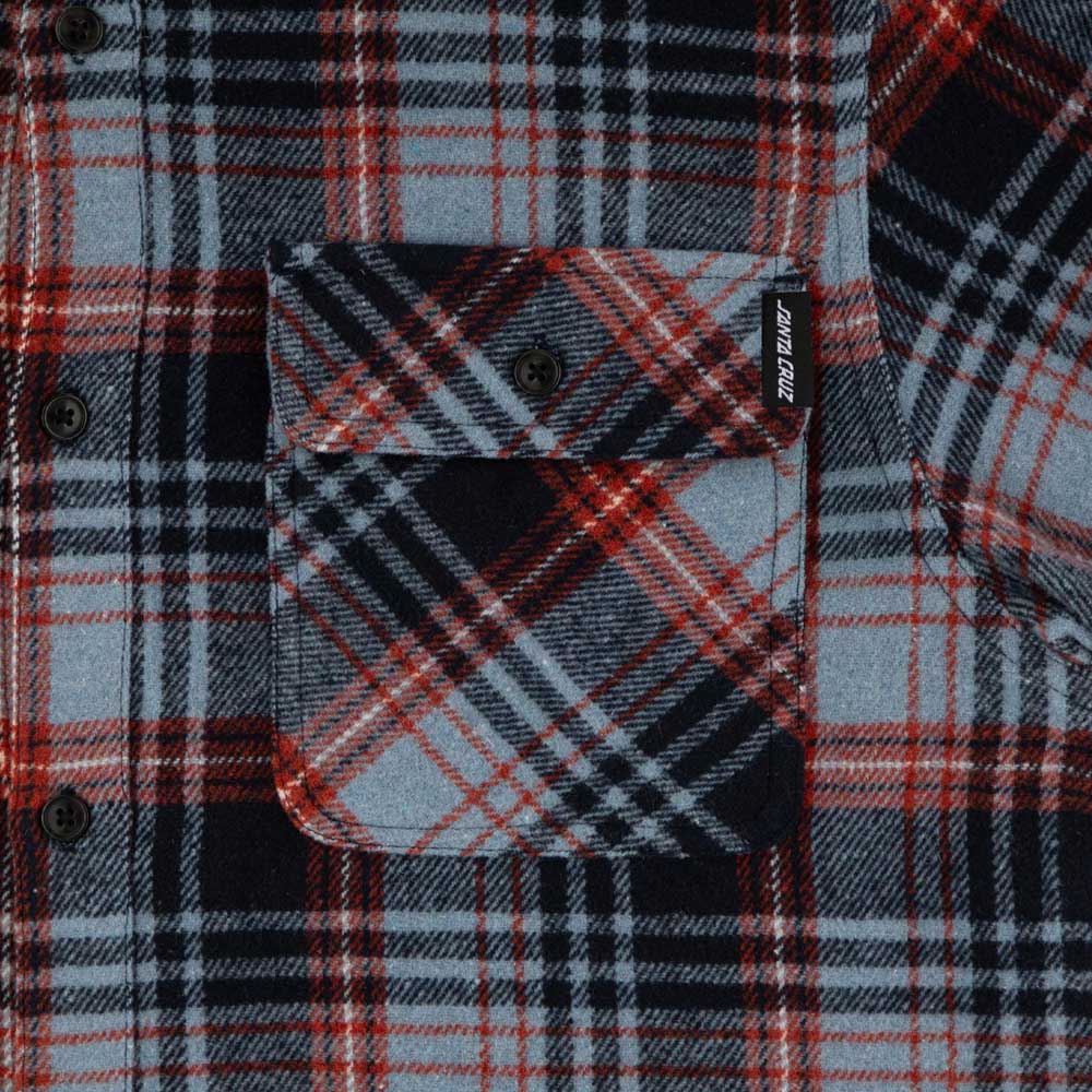 Close-up of the Classic Lonsleeve Flannel Top Blue Plaid Santa Cruz, featuring intersecting blue, black, and white plaids. The front pocket has a button and a small black tag with "Santa Cruz" in white text for signature style.