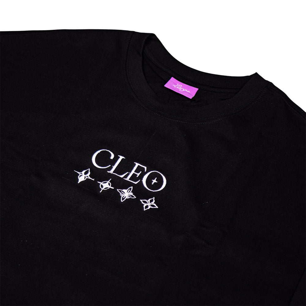 The Cleo Flame Black Tee is a black cut-n-sew T-shirt featuring the CLEO logo and four white geometric star symbols beneath it. It includes a distinctive purple neck tag and is photographed laid flat on a white background, making it an essential addition to any Cleo tees collection.