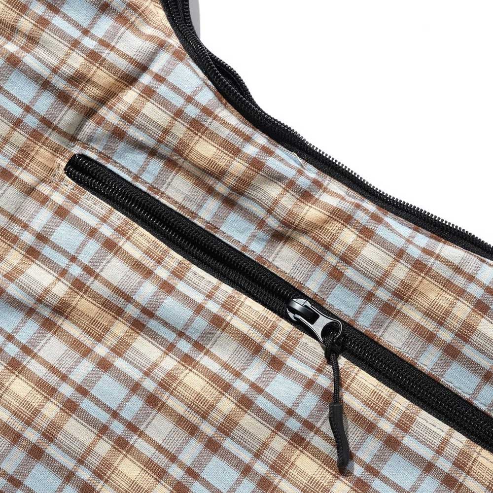 Close-up of a Sky Tan Butter Goods crossbody bag in brown, beige, and light blue plaid heavy cotton with a black zipper pocket sewn diagonally across the material and partially open.