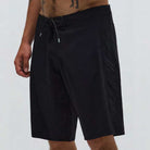 A person is shown wearing the Illusion 21 inch Trunk Black Former shorts with a drawstring waist, standing against a plain light-colored background. Only the lower torso and legs are visible.