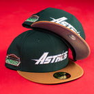 Two El Tuga Houston Astros New Era 5950 fitted hats feature green crowns, brown brims, bold white Astros logos, and a commemorative side patch. Both caps are displayed on a vibrant red background.