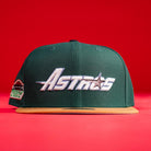 The El Tuga Houston Astros New Era 5950 Fitted Hat features a green crown, tan brim, and "Astros" in white stylized lettering on the front, displayed against a bright red background.