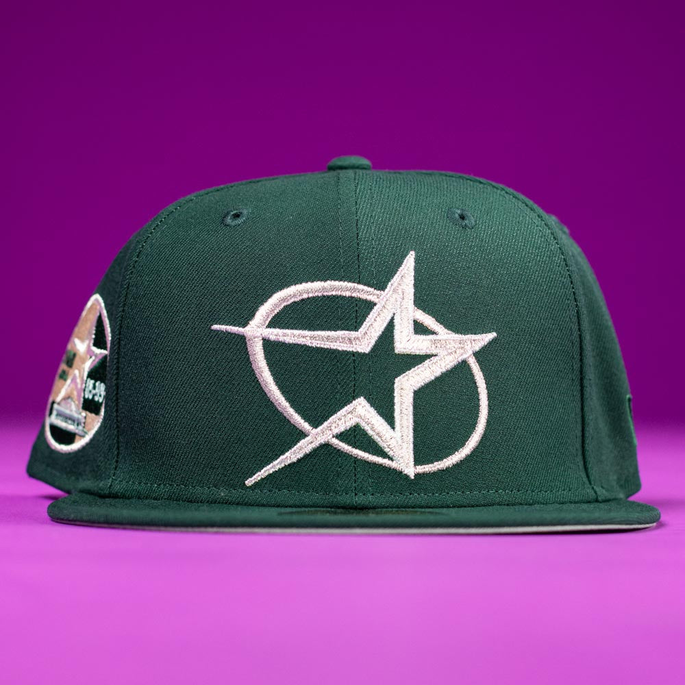 The Merc Green Silver 35th Houston Astros New Era Hat 5950 Fitted features a large white embroidered star and swoosh on the front, a left-side circular star patch, and is displayed on a solid purple background.