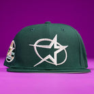 The Merc Green Silver 35th Houston Astros New Era Hat 5950 Fitted features a large white embroidered star and swoosh on the front, a left-side circular star patch, and is displayed on a solid purple background.