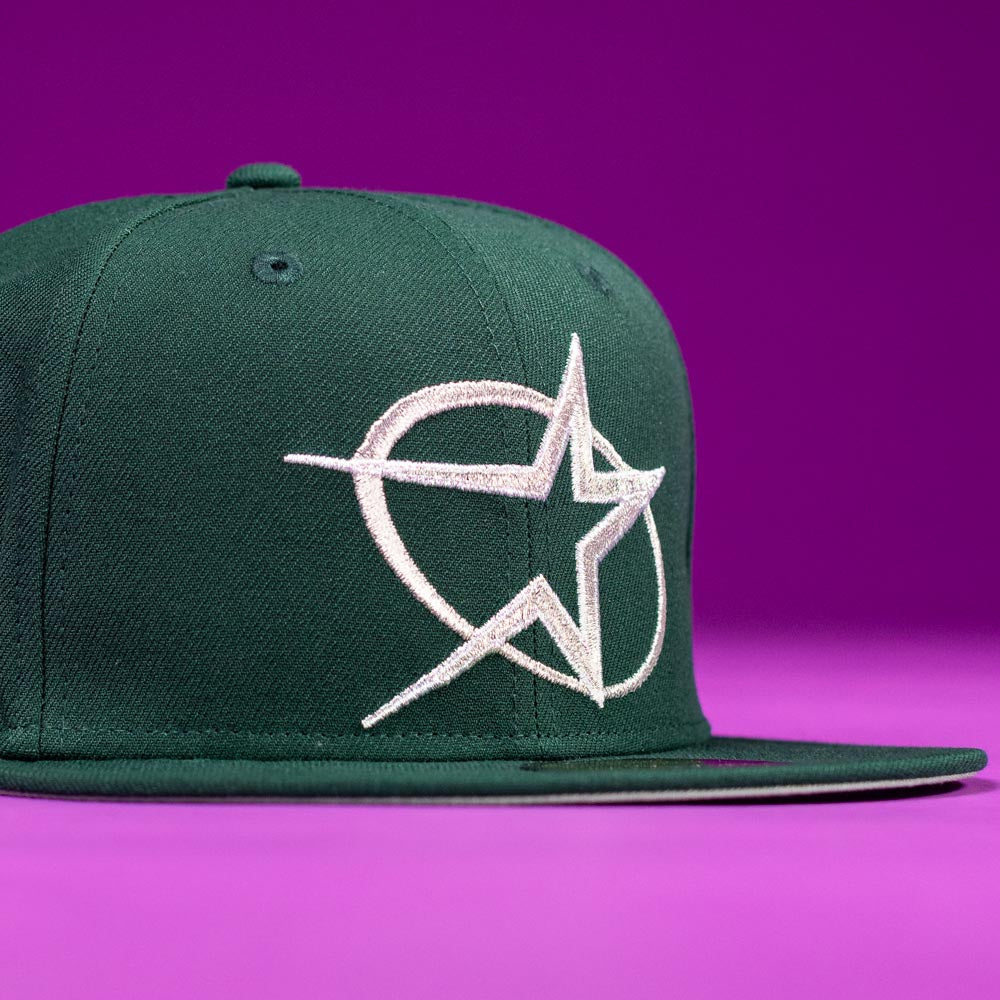 The Merc Green Silver 35th Houston Astros New Era Hat 5950 Fitted features a dark green color with a bold white star embroidered on the front, shown against a purple background.