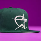 The Merc Green Silver 35th Houston Astros New Era Hat 5950 Fitted features a dark green color with a bold white star embroidered on the front, shown against a purple background.