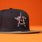 The Daikin Park Olive Houston Astros New Era 5950 Fitted Hat, featuring a tan and white star logo with an H on the front, is displayed on an orange surface with an orange background.