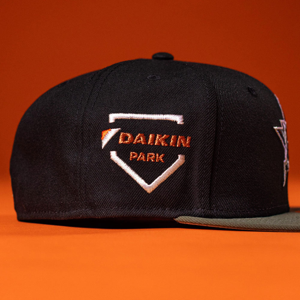 An olive New Era 5950 fitted hat, inspired by the Houston Astros, features "DAIKIN PARK" embroidered in orange and white on the side and is displayed against an orange background.