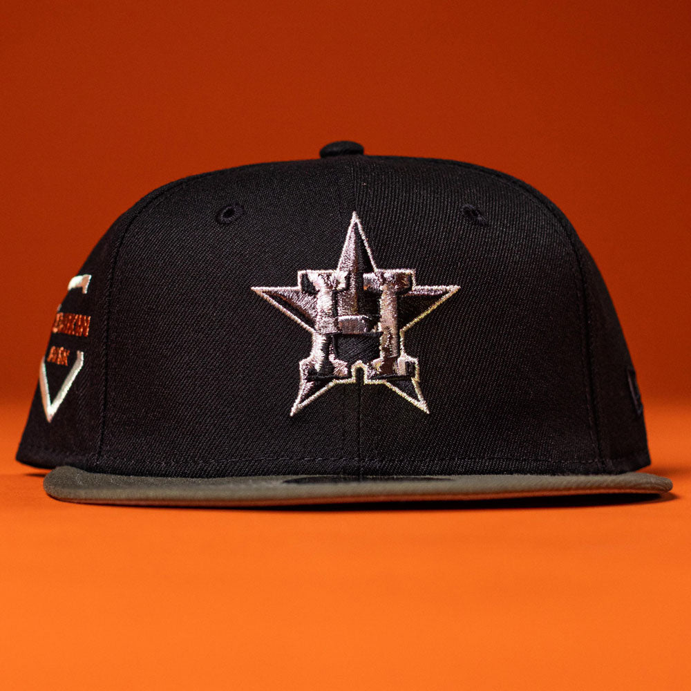 A Daikin Park Olive Houston Astros New Era 5950 Fitted Hat is displayed on an orange surface with an orange background.
