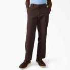 A person wearing Dark Brown Worn In Double Knee Pant A89TC0DB Dickies Skateboarding, a light blue shirt, and brown lace-up shoes stands with hands in pockets against a plain white background.