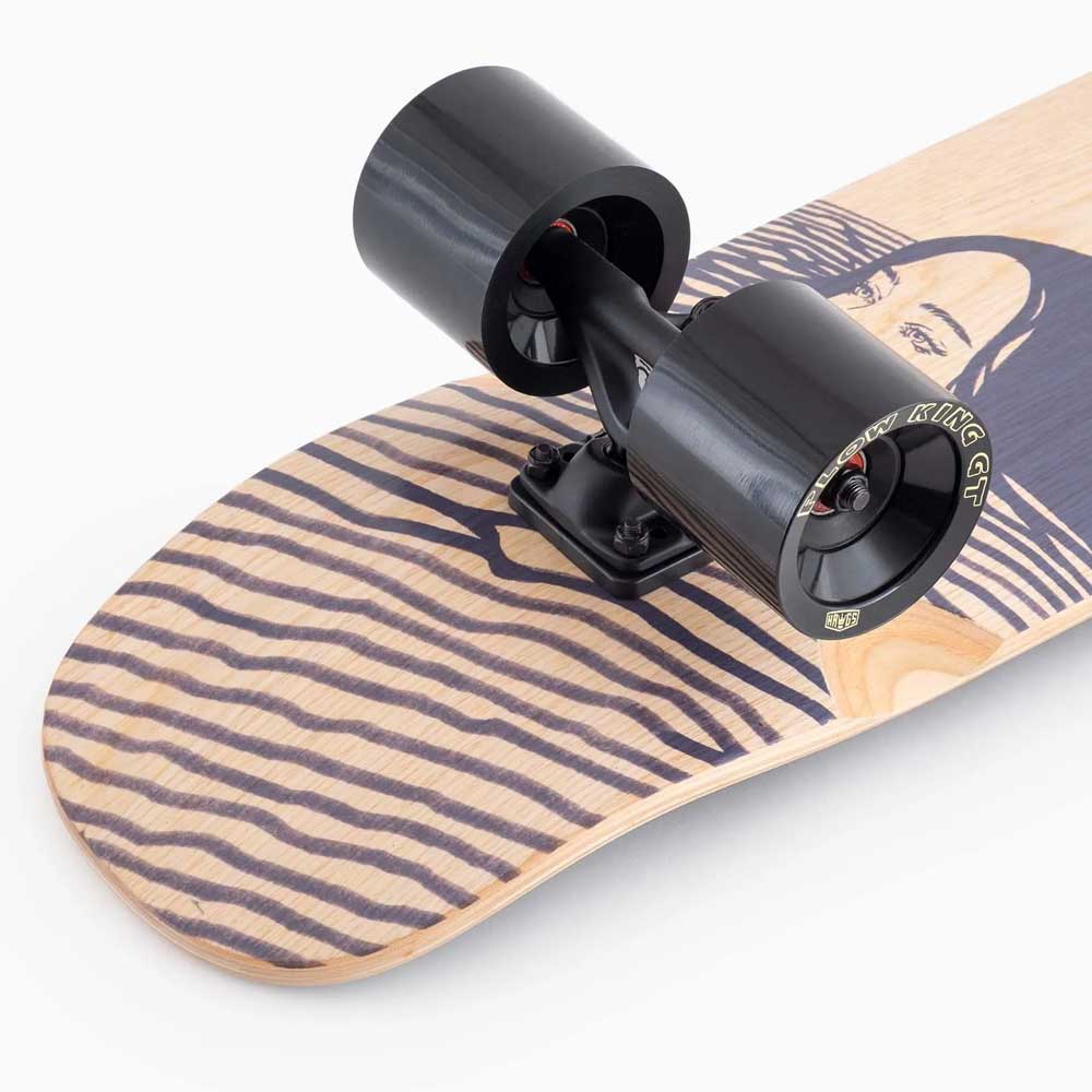 Close-up of the Dinghy Classic Fender Moray Eel Landyachtz Complete Skateboard's back end, showing molded wheel flares, large black wheels, and a wooden deck with a face graphic and wavy black lines. Trucks and wheels are prominently displayed.