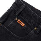 Close-up of the front pocket of Distressed Flat Black Relaxed Denim Jeans by Butter Goods, made from 100% cotton denim with brass rivets, an orange Butter label, and a relaxed fit silhouette.