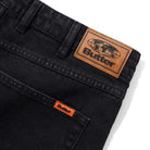 Close-up of Distressed Flat Black Relaxed Denim Jeans by Butter Goods, made from 100% cotton, featuring a brown leather Butter patch with globe graphic and an orange Butter tag above the front pocket.