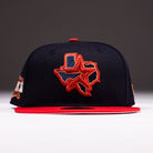 The El Karma ASG Navy Red Houston Astros New Era Hat 5950 Fitted features a navy and red color scheme, inspired by the Astros, with an embroidered Texas state outline and star on the front. The bill is red, and additional small patches appear on the sides.