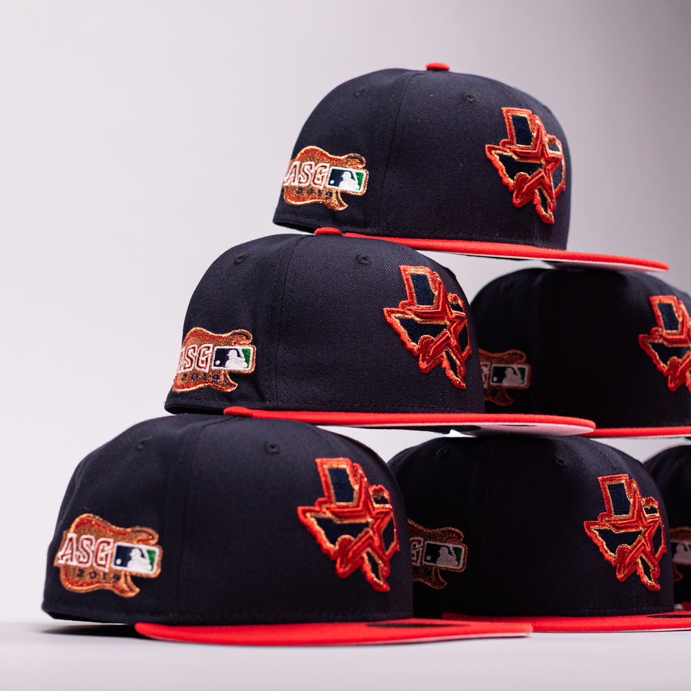 Six El Karma ASG Navy Red Houston Astros New Era Hat 5950 Fitted caps by New Era are stacked in two pyramids. Each cap showcases a navy blue crown with a red brim, decorated with a Texas state patch, “ASG” initials, and a small MLB logo on the side to celebrate the Houston Astros—all arranged against a light gray background.