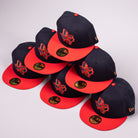 Six El Karma ASG Navy Red Houston Astros New Era 5950 Fitted hats are stacked in a pyramid. Each cap features a navy blue crown, red brim, colorful embroidered Texas state outline, and a sticker on the brim. The background is light gray.