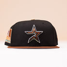 A black Espresso Martini Houston Astros New Era 5950 Fitted Hat featuring a metallic gold outlined star logo on the front and a brown brim, displayed against a neutral background. This cap by Alyyjadee adds a touch of standout style to any look.