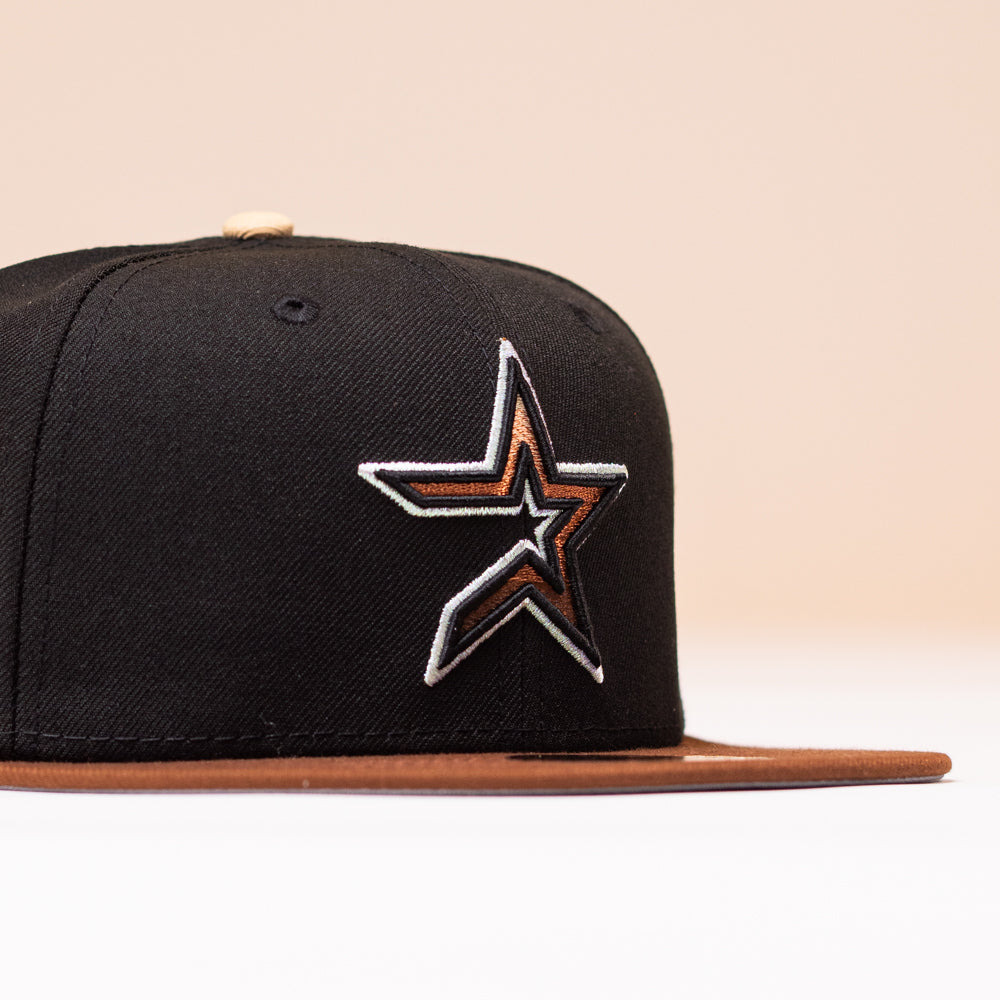 The Espresso Martini Houston Astros New Era Hat 5950 Fitted is a black fitted cap with a brown brim, highlighted by a star-shaped patch with silver and brown outlines on the front left side—reminiscent of classic Astros designs. Set against a soft beige background, the hat exudes an Alyyjadee-inspired aesthetic.