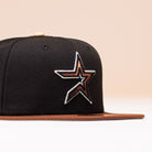 The Espresso Martini Houston Astros New Era Hat 5950 Fitted is a black fitted cap with a brown brim, highlighted by a star-shaped patch with silver and brown outlines on the front left side—reminiscent of classic Astros designs. Set against a soft beige background, the hat exudes an Alyyjadee-inspired aesthetic.