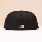 Back view of the Espresso Martini Houston Astros New Era Hat 5950 Fitted, featuring a small orange MLB logo embroidered near the bottom edge. This cap combines sleek style with authentic team detail.