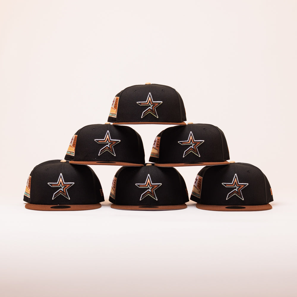 Six black and brown caps with star logos, including the Espresso Martini Houston Astros New Era Hat 5950 Fitted, are stacked in a pyramid shape against a plain light background.