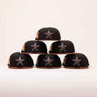 Six black and brown caps with star logos, including the Espresso Martini Houston Astros New Era Hat 5950 Fitted, are stacked in a pyramid shape against a plain light background.