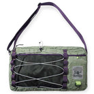 The Express Side Bag Sage by Butter Goods is a rectangular gray and purple nylon bag with a mesh front pocket, bungee cord, adjustable strap, 15L capacity, and a BUTTER logo patch with globe graphic on the lower right corner.