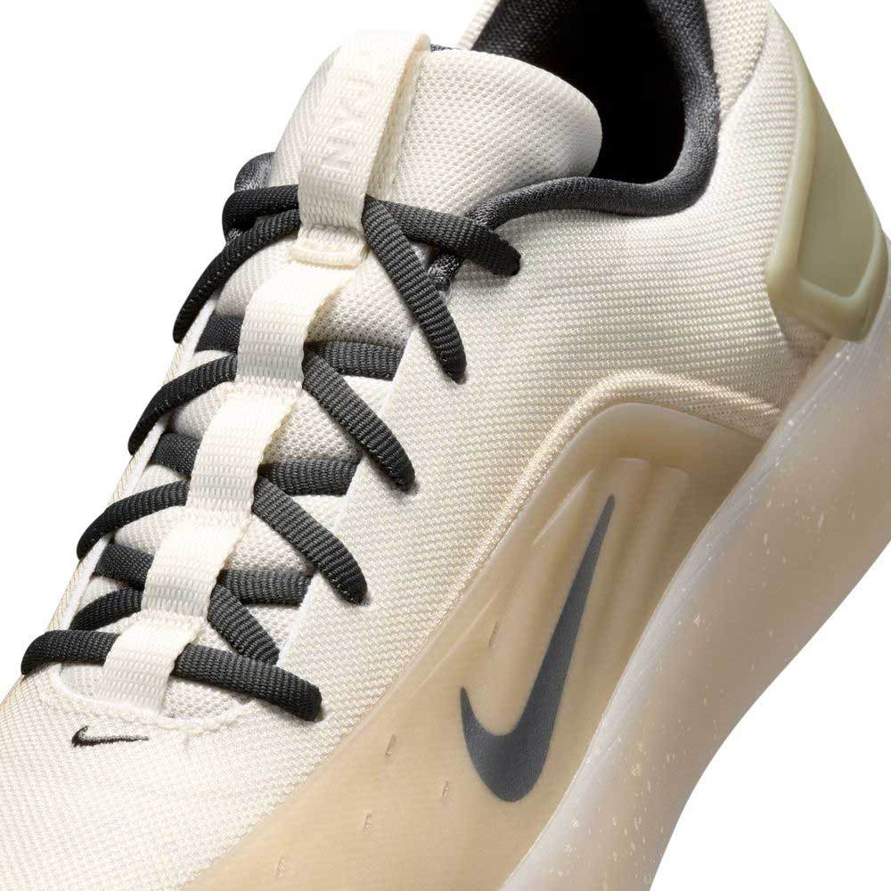 A close-up of the FQ1273-200 Khaki White Zoom Nyjah 4 Nike SB skateboarding shoe, featuring a beige colorway, black laces, translucent sole, black swoosh, Air Zoom cushioning for comfort, and a modern minimalist design.
