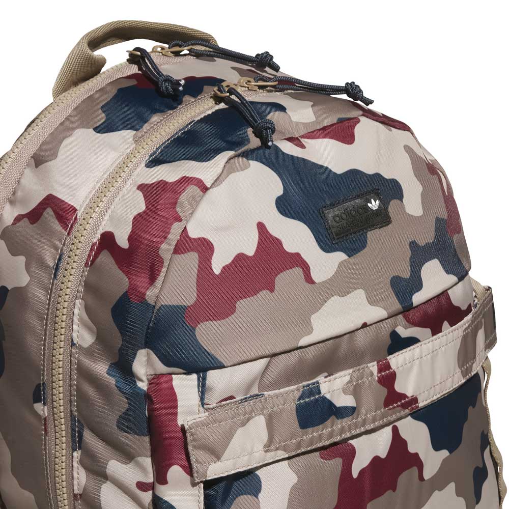 Close-up of the FSBS Backpack KS6815 Khaki Camo by adidas Skateboarding, displaying a camouflage pattern in shades of tan, maroon, navy, and beige. This backpack features a front zippered pocket and a small black logo patch near the top.