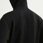 A person is shown from the back wearing a Nike SB Fleece Pullover Black White IF0655010 hoodie with a relaxed fit. Only the hood, upper back, and shoulders are visible against a plain light background.