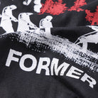 Close-up of the Engineered Former Tee in Washed Black, showcasing its vintage black 200GSM cotton fabric with white printed silhouettes of people holding objects and bold FORMER lettering, accented by red screen print details in the background.
