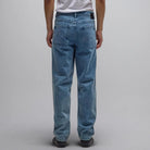 A person wearing the Crux Denim Pant Washed Blue Former—light blue, straight-fit jeans made from 100% cotton denim—and a white t-shirt stands facing away from the camera against a plain gray background.