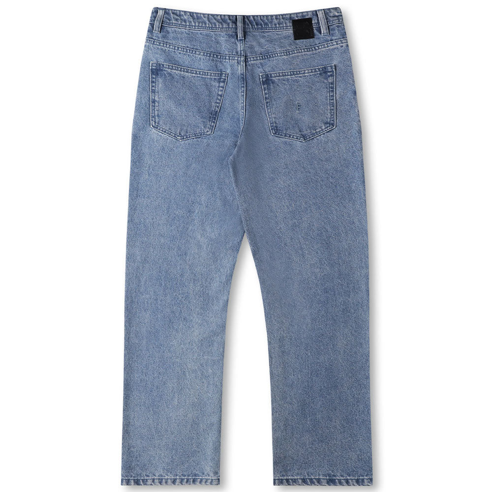 A pair of Crux Denim Pant Washed Blue Former jeans shown from the back, featuring a classic straight fit silhouette, two rear pockets, and a black leather patch on the waistband. Crafted from 100% cotton denim for lasting comfort and durability.