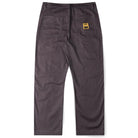 The Reynolds Work Pant Gunmetal Former is shown from the back in dark gray cotton twill, featuring two large rear pockets—one adorned with a small yellow rectangular patch with a black logo. These baggy work pants are inspired by Dane Reynolds’ signature relaxed style.
