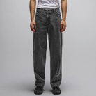A person stands facing forward against a plain light background, wearing a white t-shirt and the Crux Denim Pant Washed Black Former—loose-fitting, straight-fit jeans crafted from 100% cotton denim for comfort and durability. The person’s head is not visible.