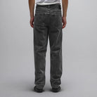 A person wearing a white t-shirt and loose-fitting, straight fit Crux Denim Pant Washed Black Former made from 100% cotton denim stands facing away from the camera against a plain light gray background.