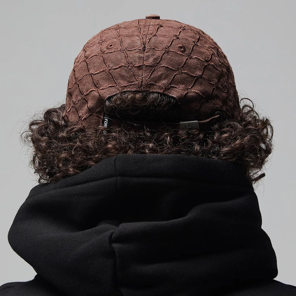A person with curly hair is seen from the back against a plain gray background, wearing the Alleviate Cap Former Hat Bark—a textured brown cap—and a black hoodie crafted from premium 200GSM cotton.