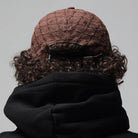 A person with curly hair is seen from the back against a plain gray background, wearing the Alleviate Cap Former Hat Bark—a textured brown cap—and a black hoodie crafted from premium 200GSM cotton.